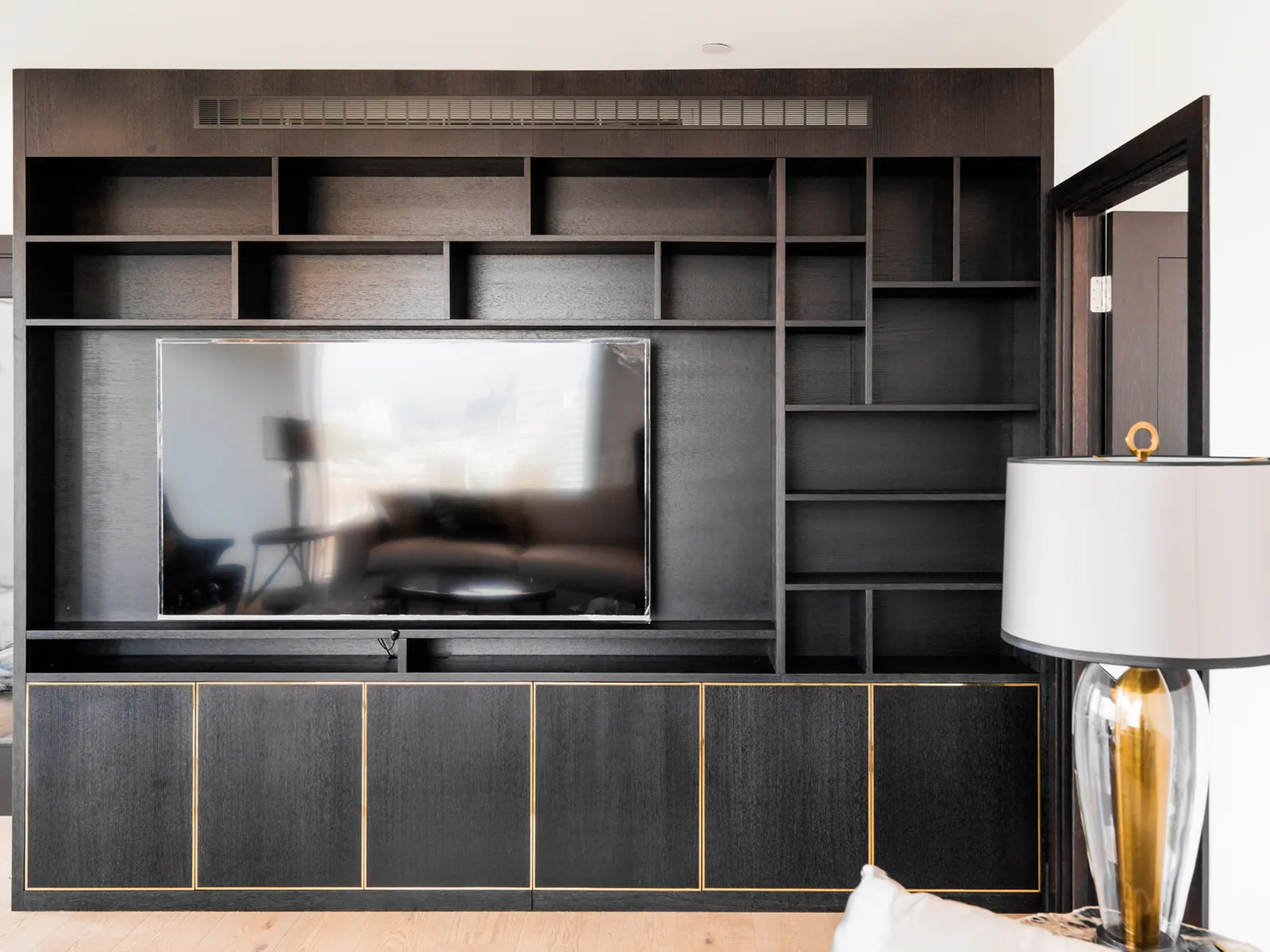 Black oak-grain bespoke media wall with integrated television and brass-toned inlay