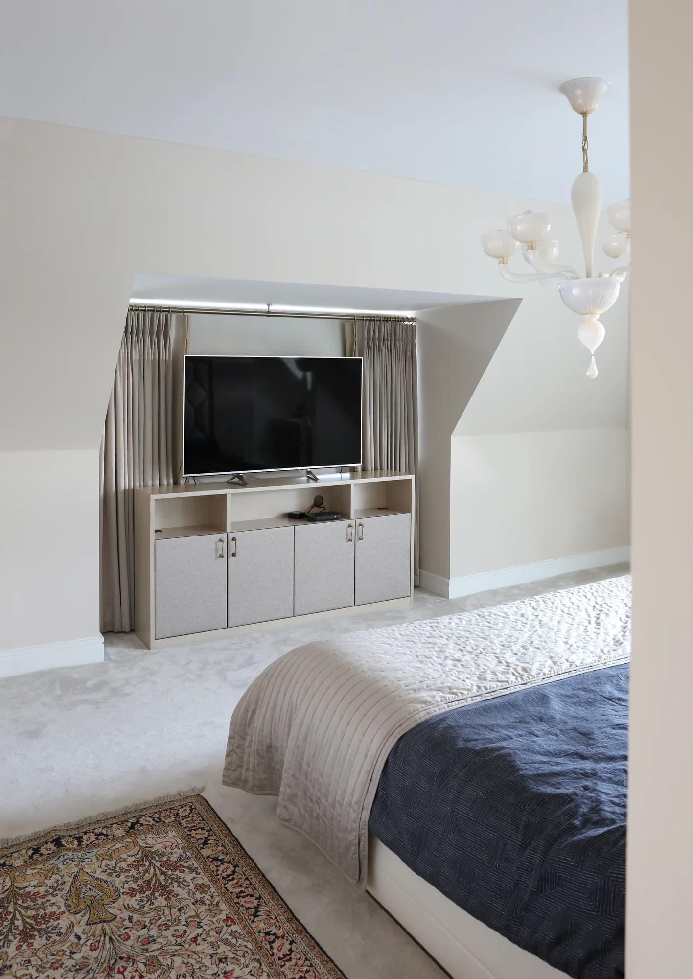 Bedroom TV cabinet beneath a sloping ceiling with open shelves and pale lower cupboards