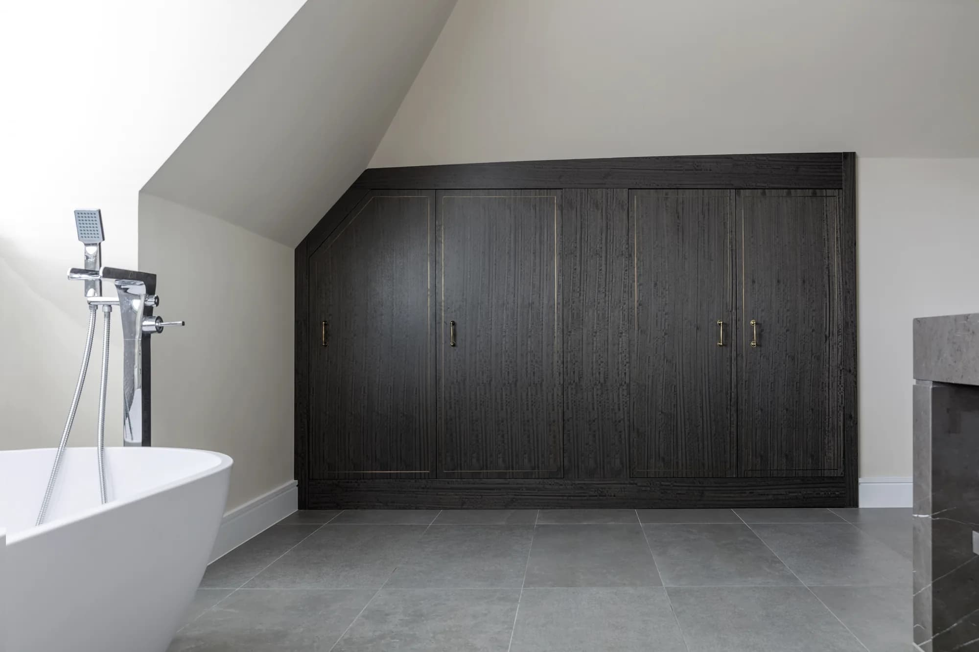 Dark bathroom cupboards with closed doors shaped beneath a sloping ceiling