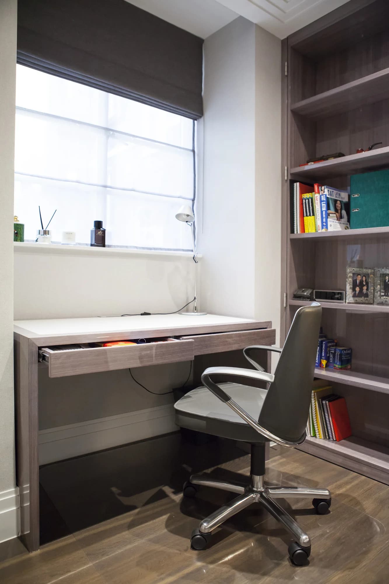 Fitted bedroom desk beneath a window beside a tall bookcase, with its drawer open