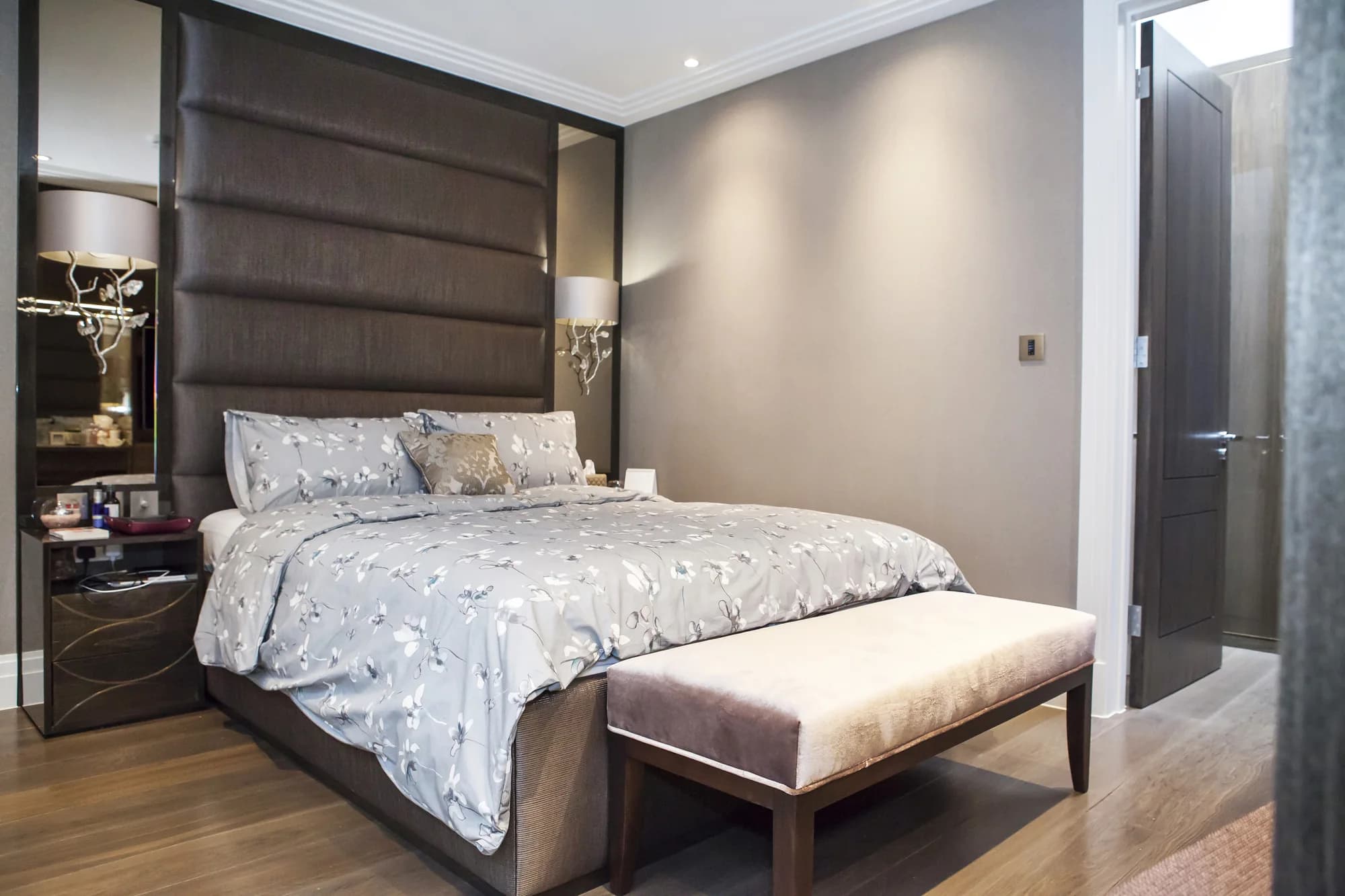 Tall padded headboard with reflective side panels and dark bedside cabinets