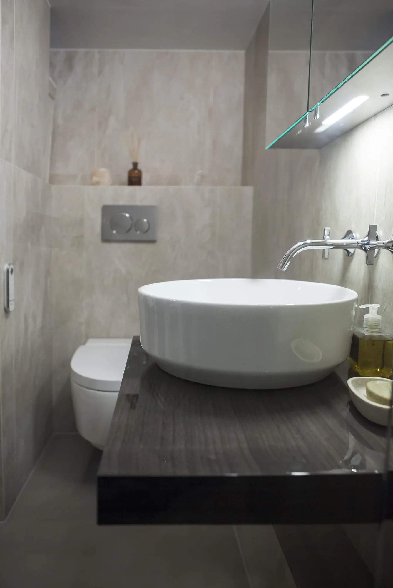 Round white basin on a dark floating vanity shelf in a compact bathroom